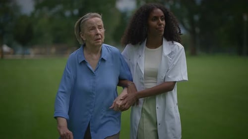 Caring Young Woman Walking with Elderly Woman Outdoors