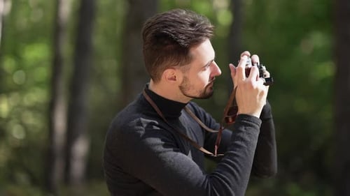 Side View Portrait of Smiling Caucasian Young Man Taking Photos of Nature with Camera Standing in