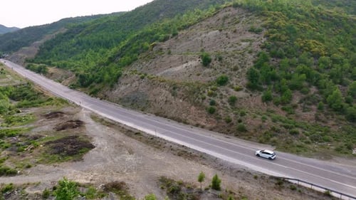 Aerial View of Cars Driving on a Highway Through Green Hilly Farmland with Small Buildings and