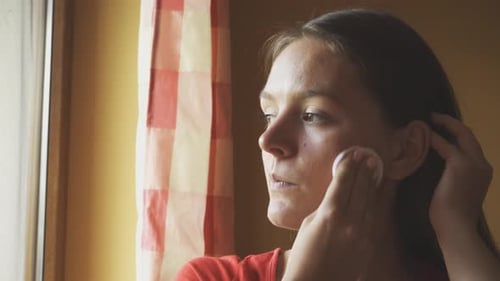 Young Woman Applying Makeup with Cotton Pad Indoors