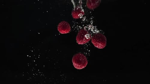 Fresh healthy food. Red raspberries falling into water on black background. Fresh fruits splashing