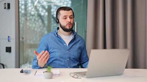 Man with headset video-calling on laptop in office