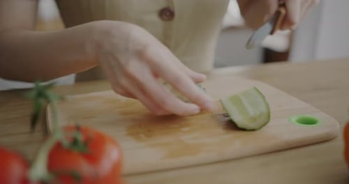 Closeup of Female Hand Preparing Vegetable Salad Cutting Cucumber Making Lunch at Kitchen Table