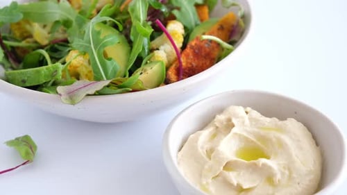 Dipping Cauliflower in Hummus Next to Healthy Salad