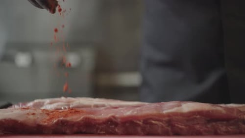 Close Up Slow Motion Video of a Chef Peppering Raw Ribs with Red Pepper