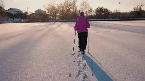 Senior Woman Practicing Nordic Walking on a Frozen Lake at Sunset Enjoying an Active and Healthy