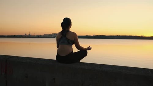The Girl Meditates in the Lotus Position on the Lake at Sunset
