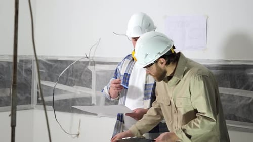 Two Architects Analyze a Drawing of a Building While Standing Indoors