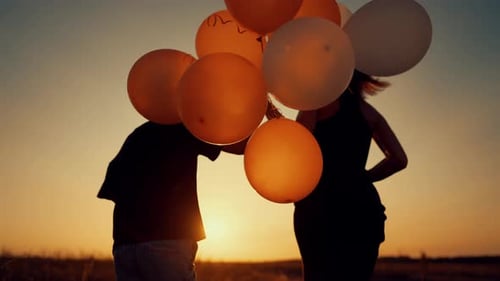 Child and adult silhouette running with balloons at sunset