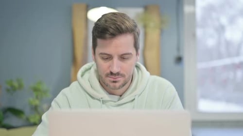 Close Up of Young Man Smiling at Camera while using Laptop