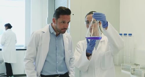 Female scientist analyzing liquid in conical flask with a male colleague