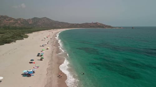Drohnenflug über plätschernde Wellen, während sich Touristen an einem sonnigen Tag entspannen und den tropischen Strand genießen