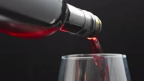 I pour red wine into a glass, on a black background. close-up.
