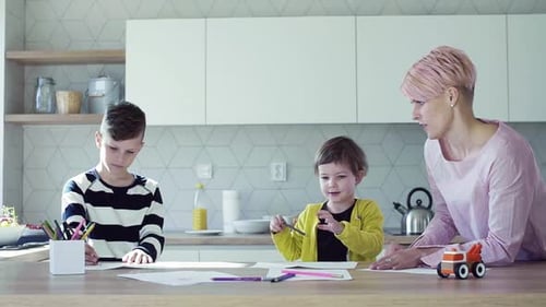 Woman and two children drawing at kitchen counter