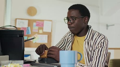 Man Eats Sandwich at Desk, Computer in Office
