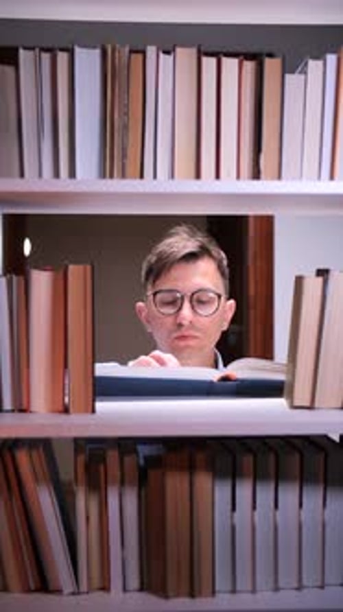 Vertical Video Young Student Reading a Book Between Bookshelves in Library