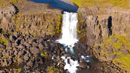Slow establishing shot of a waterfall flowing over a cliff in the vast Icelandic countryside