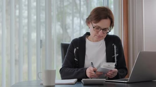 Woman Checking Bills Taxes Bank Account Balance and Calculating Expenses in the Living Room at Home