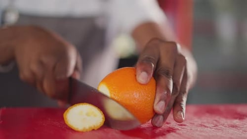 Black Man Cuts Orange on Table Closeup