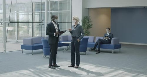Business people in office meeting in lobby wearing protective face mask and using digital tablet