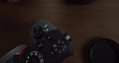 Camera body and lens on wooden table, close up top down dolly forward shot