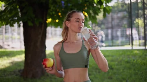 Young Woman Drinking Water with an Apple Outside