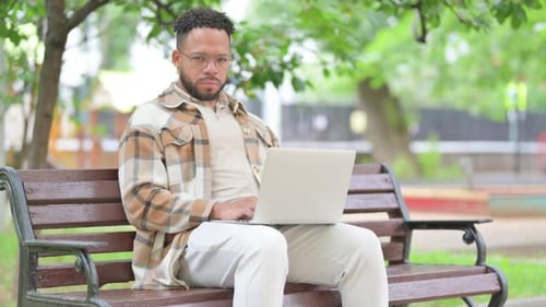 Serious Hispanic Man with Laptop on Park Bench