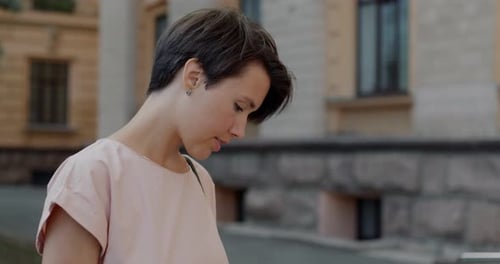 Portrait of Carefree Young Lady Looking Down Then Turning to Camera and Smiling in City Downtown