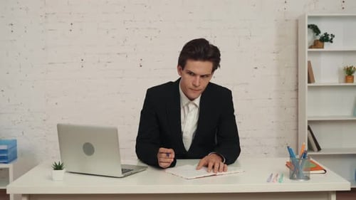 Medium Video of a Young Man Sitting at the Desk in the Office He Writes Something Down Crossed That