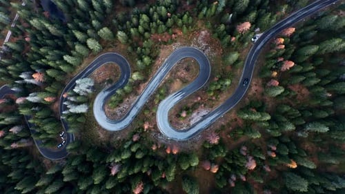 Winding mountain road through dense forest in autumn colors, aerial view from high above