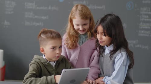 Three Happy Elementary Age Children Looking at Tablet