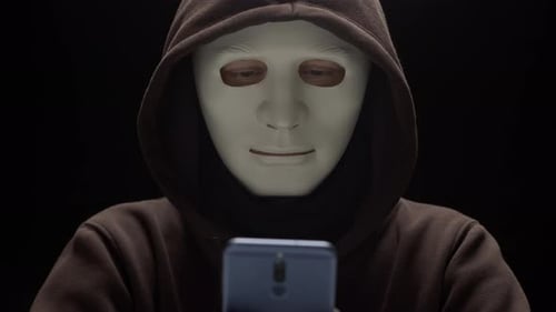 Hooded Figure in Mask Using Cell Phone