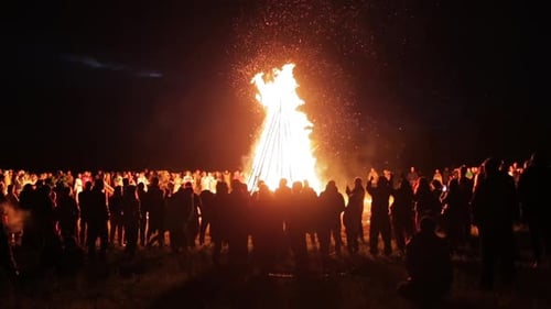 Eine große Menschenmenge feiert in der Nähe eines riesigen Lagerfeuers Brennende heiße Funken steigen aus einem großen Feuer in