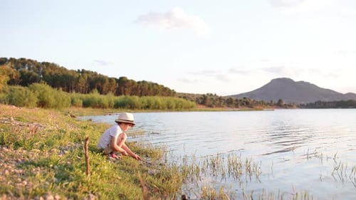 Petit garçon curieux jouant avec un bâton au bord d'un lac calme