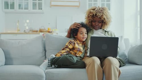 Black Mother Hugging Little Son and Discussing Something on Laptop at Home