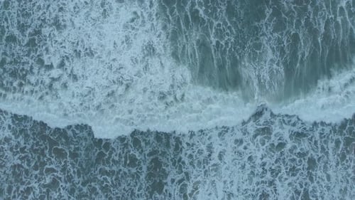High overhead drone shot captures the textures of water as sea waves crush, foam, bubble, and swirl