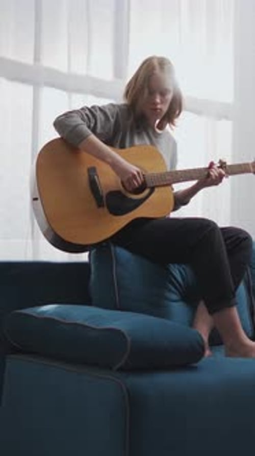 Teen Girl Plays Acoustic Guitar on Cozy Sofa