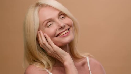 Middle Aged Happy Mature Old Caucasian 50s Woman Flirty Looking at Camera in Beige Studio Smiling