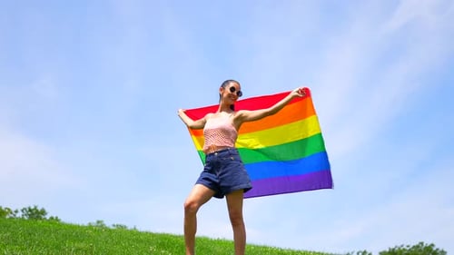 Young Woman Smiles Holding Rainbow Flag Outdoors