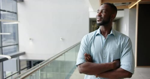 Smiling businessman standing confidently with arms crossed in modern office hallway, copy space