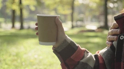 Person Holds Coffee Cup Outside on Sunny Day