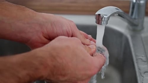 A Person Diligently and Carefully Cleaning Numerous Utensils Under a Steady Flow of Running Water in