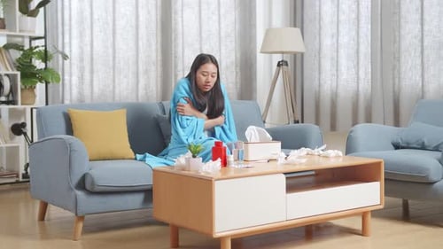 Femme asiatique malade avec une couverture ayant froid sur le canapé dans le salon à la maison