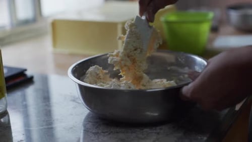 Gooey dough mixture being pressed and kneaded by spoon in steel bowl, filmed as close up slow motion