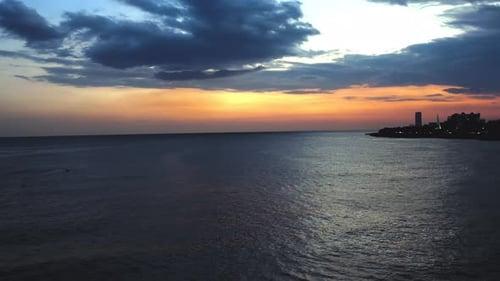 Drone footage at dusk over the Sea with seagulls flying and the city in the background