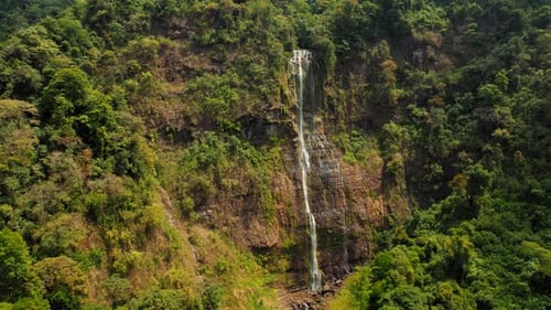 Tall waterfall cascading down rocky cliff in lush green jungle of Costa Rica