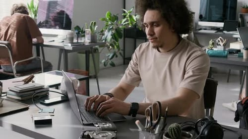 Porträt eines jungen männlichen Entwicklers, der auf einem Laptop programmiert und in die Kamera schaut