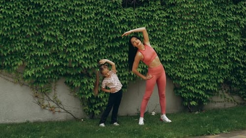 Mother and Daughter Stretching Exercises Outdoors in a Lush Garden Setting