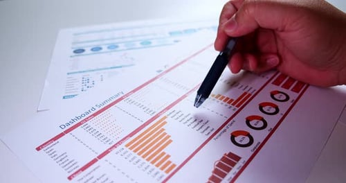 Close-up of businessman's hands with pen working at office desk and analyzing dashboard graphs and c