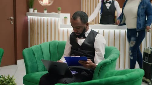 Man Taking Notes in Hotel Lobby on Laptop
